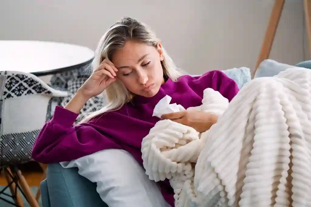 Imunitate scăzută la adulți – Cauze și soluții eficiente Tânără adultă cu simptome de imunitate scăzută stând în pat cu oboseală și răceală ușoară