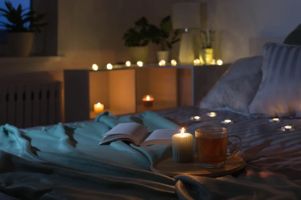 Cană de ceai pt somn pe un pat confortabil, cu lumânări aprinse și o carte deschisă – atmosferă de relaxare înainte de culcare