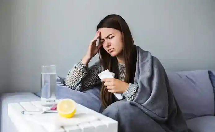Femeie cu imunitate scăzută stând pe canapea cu febră și oboseală – simptome frecvente ale unui sistem imunitar slăbit